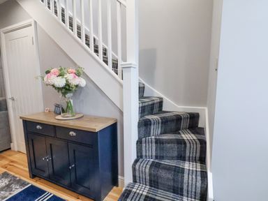 A staircase with plaid carpet next to a wooden cabinet with flowers on top at The Dollhouse in Cayton Bay