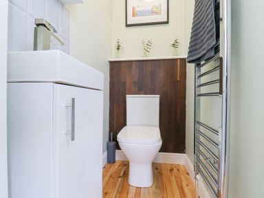 A bathroom with a white toilet and sink cabinet a metal towel rack with a dark towel and three small vases on a shelf at The Dollhouse in Cayton Bay