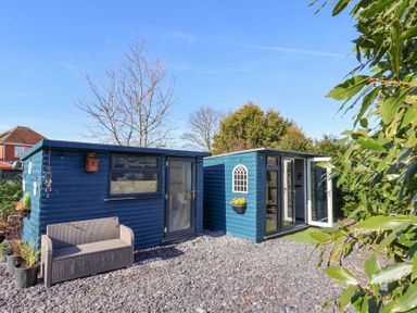 Two blue garden sheds with a bench and potted plants outside at The Dollhouse in Cayton Bay