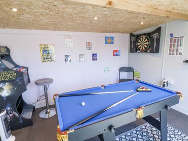 A game room with a pool table a dartboard a Star Wars arcade machine and posters on the wall at The Dollhouse in Cayton Bay