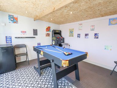 A game room with a pool table arcade machine and posters on the walls at The Dollhouse in Cayton Bay