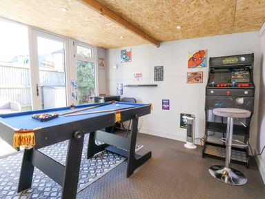 A game room with a pool table an arcade machine and stools at The Dollhouse in Cayton Bay