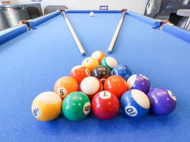 A blue pool table with pool balls arranged in a triangle and two pool cues resting on the table at The Dollhouse in Cayton Bay