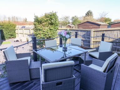 A patio with a glass table and six cushioned chairs with flowers on the table at The Dollhouse in Cayton Bay