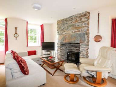 A living room with a stone fireplace a beige recliner a grey sofa and a wooden coffee table at Ty Nain in Beddgelert