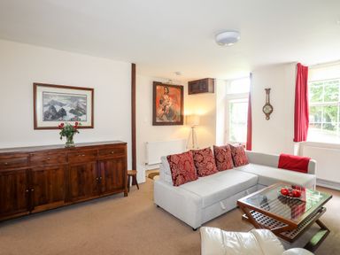 A living room with a gray sofa and red cushions a wooden sideboard with flowers and two paintings at Ty Nain in Beddgelert