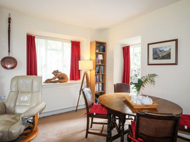 A dining room with a round wooden table and chairs with red cushions and a cream armchair at Ty Nain in Beddgelert