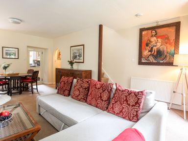 A living room with red patterned cushions on a sofa a painting on the wall and a dining table at Ty Nain in Beddgelert
