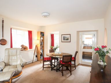 A dining room with a round wooden table with four chairs and red cushions and a beige leather recliner chair at Ty Nain Beddgelert