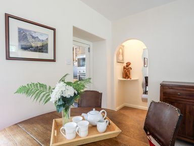 A dining room with a wooden table set with a tea set and flowers a painting on the wall and a wooden cabinet at Ty Nain in Beddgelert