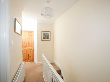 A hallway with a wooden door a small framed picture on the wall and a white banister at Ty Nain in Beddgelert