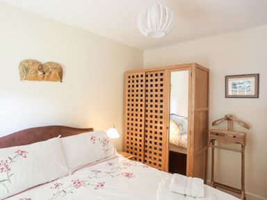 A bedroom with a bed with floral bedding a wooden wardrobe with a mirror and a wooden clothes stand at Ty Nain in Beddgelert