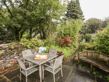 An outdoor patio area with a metal table and chairs a wooden bench and surrounding greenery at Ty Nain in Beddgelert