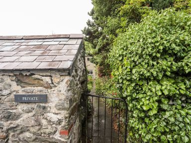 A stone wall with a private sign and a metal gate next to green bushes at Ty Nain in Beddgelert