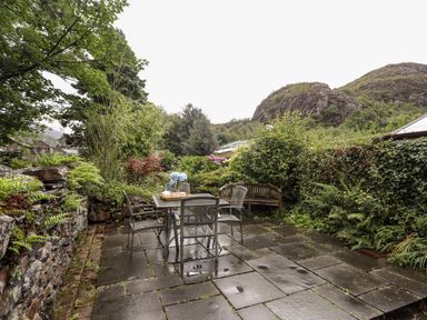 An outdoor patio with a table and four chairs surrounded by plants and stone walls at Ty Nain in Beddgelert