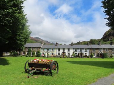 A row of stone and painted houses with chimneys and a large green lawn with a flower planter on wheels at Ty Nain in Beddgelert