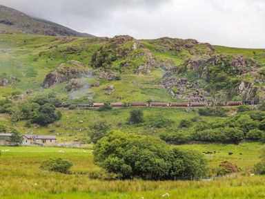 A rural landscape with a steam train passing through grassy hills and rocks at Ty Nain in Beddgelert