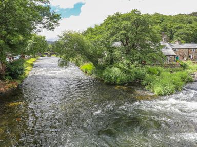 A river flowing through a village with trees and stone houses by the banks at Ty Nain in Beddgelert