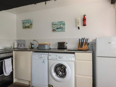 A kitchen with a stove a dishwasher a washing machine a refrigerator a sink knives in a block and two paintings on the wall at Chy Rani in Portmellon near Mevagissey