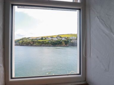 A window with a view of water and houses on a hill at Chy Rani in Portmellon near Mevagissey