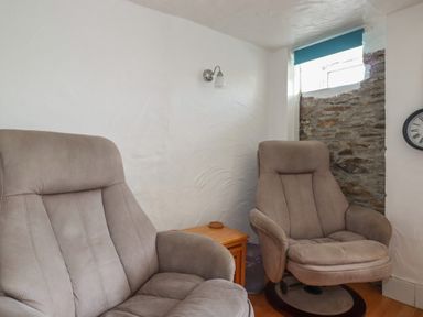 Two armchairs with a wooden table between them in a room with white walls and a small window at Chy Rani in Portmellon near Mevagissey