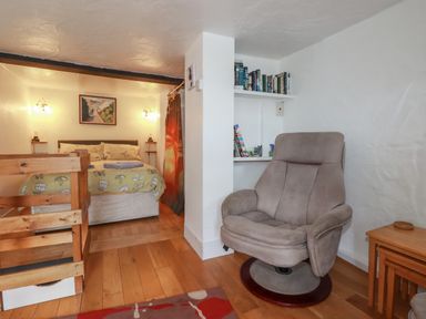A bedroom with a bed and side tables next to a reading chair and small tables at Chy Rani in Portmellon near Mevagissey