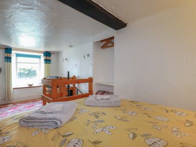A bedroom with a bed covered in a yellow floral bedspread with folded towels on top and a window with curtains at Chy Rani in Portmellon near Mevagissey