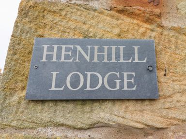 A black plaque with white text reading Henhill Lodge attached to a stone wall at Henhill Lodge in Chathill near Seahouses