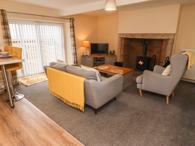 A living room with grey sofa and armchair a wooden coffee table a fireplace and a TV at Henhill Lodge in Chathill near Seahouses