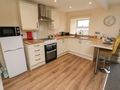 A kitchen with white cabinets a refrigerator a stove a microwave a sink and a breakfast bar with yellow chairs at Henhill Lodge in Chathill near Seahouses