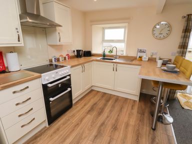 A kitchen with white cabinets a stove a sink a wooden countertop and a breakfast bar with yellow stools at Henhill Lodge in Chathill near Seahouses
