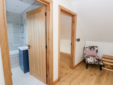 A bathroom with a bathtub and shower, and a chair outside at Beudy near Llanilar