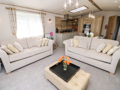 A living room with two beige sofas a beige ottoman with flowers and a kitchen in the background at 7 Wild Haven in Landford