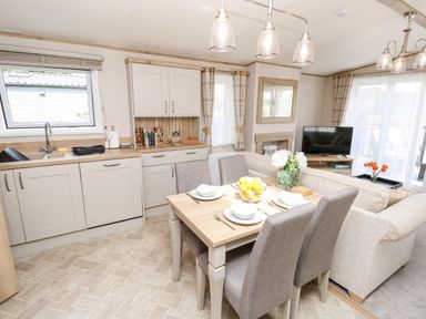 A kitchen and dining area with a table set for four, a living room with a sofa and TV at 7 Wild Haven in Landford