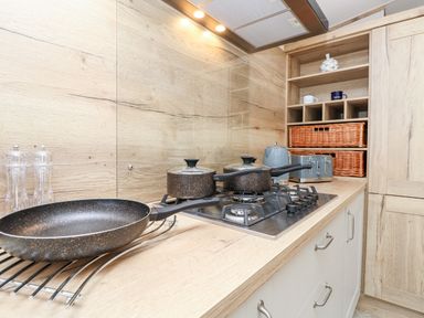A kitchen countertop with a gas stove frying pan pots salt and pepper grinders a kettle toaster baskets and shelves at 7 Wild Haven in Landford