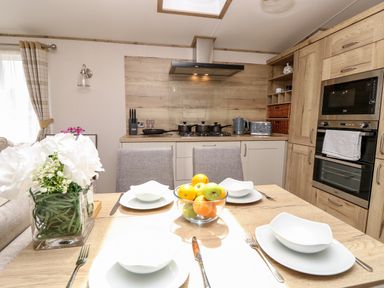 A kitchen with wooden cabinets a dining table set with white dishes a bowl of fruit and a flower vase at 7 Wild Haven in Landford