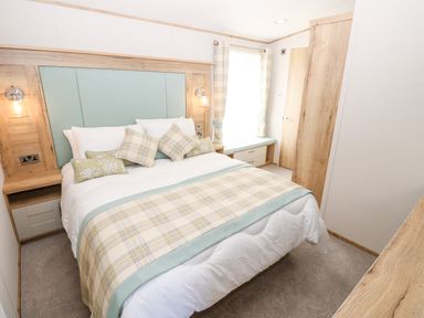A bedroom with a double bed with pillows and a plaid bed runner beside a window with curtains and built in storage at 7 Wild Haven Landford