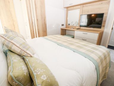 A bedroom with a bed pillows a plaid bed runner a TV on a wooden dresser and a small mirror at 7 Wild Haven in Landford