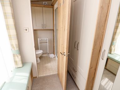 A small bathroom with a toilet and towel radiator next to a wardrobe with mirrored door and a window seat with cushions at 7 Wild Haven in Landford
