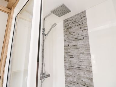 A shower area with a chrome showerhead and handheld shower against a wall with grey stone tiles at 7 Wild Haven in Landford