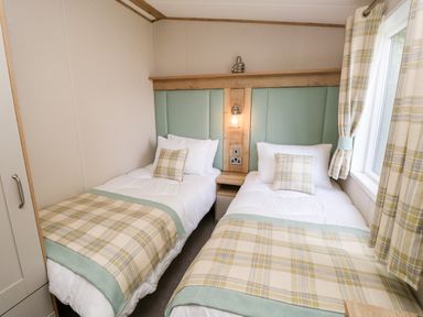 A bedroom with two single beds with plaid bed runners and pillows a small nightstand with a lamp between beds and a window with matching plaid curtains at 7 Wild Haven in Landford