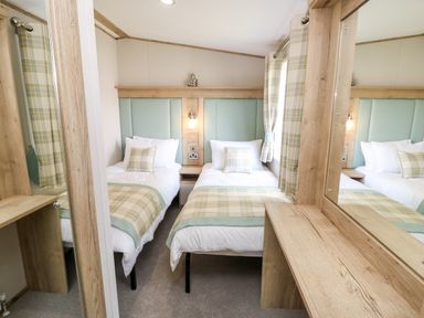 A bedroom with two single beds with plaid bedding and pillows a wooden desk and mirror at 7 Wild Haven in Landford