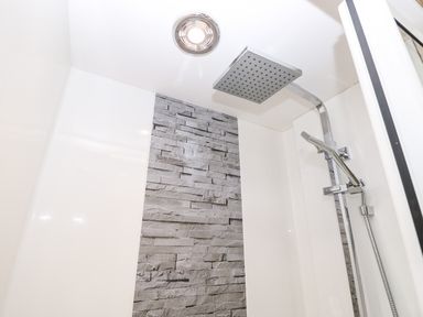 A shower area with a square rainfall showerhead and a handheld shower on a metal rail with stone tile accent at 7 Wild Haven in Landford