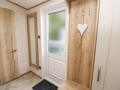 A hallway with a white door a full length mirror coat hooks and a wooden bench at 7 Wild Haven in Landford