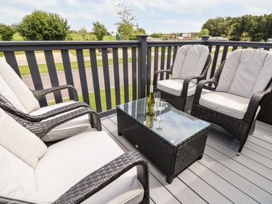 An outdoor patio with four cushioned wicker chairs and a glass-top wicker table with wine and glasses at 7 Wild Haven Landford
