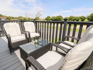 An outdoor patio with four wicker chairs and a glass-top table with a bottle and two glasses at 7 Wild Haven in Landford