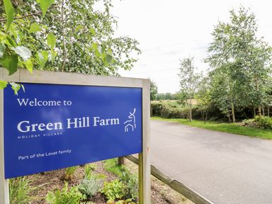 A blue welcome sign for Green Hill Farm holiday village near a road and trees at Green Hill Farm in Landford