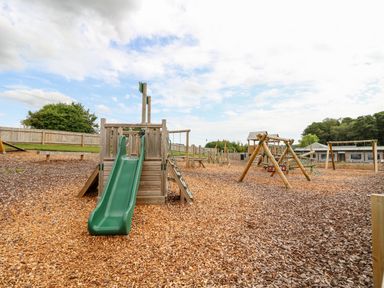 A playground with a green slide wooden climbing structures and swings at 7 Wild Haven in Landford