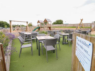An outdoor seating area with tables and chairs next to a children's playground with wooden play structures and slides at 7 Wild Haven in Landford