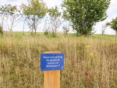 A blue reserved parking sign on a wooden post in front of tall grass and small trees at 7 Wild Haven in Landford